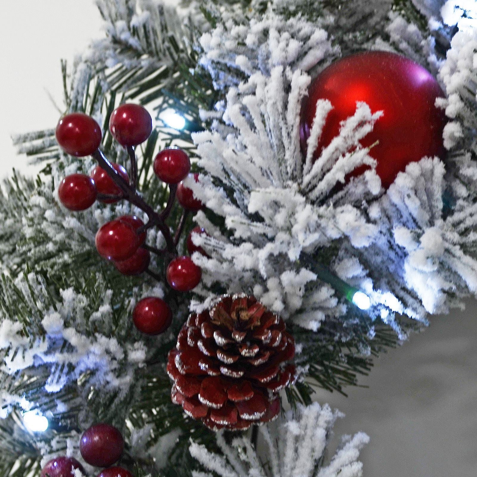 close up of snow flocked frosted wreath with red baubles, berries and silver pine cones